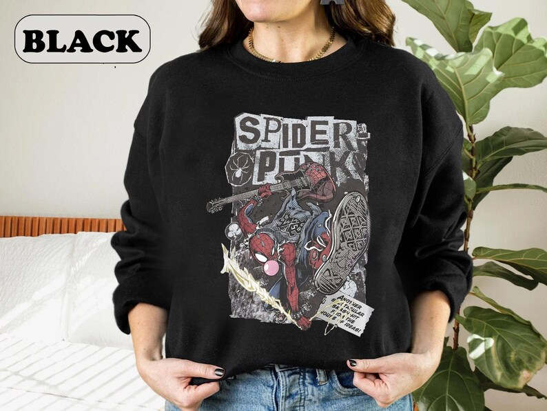 Peut inclure: Sweat-shirt noir avec un motif Spider-Man et l'inscription "SPIDER PUNK" dans une police de caract&egrave;res us&eacute;e. Le motif comprend une guitare et une bulle de dialogue. Le mot "BLACK" est dans un ovale blanc en haut &agrave; gauche.