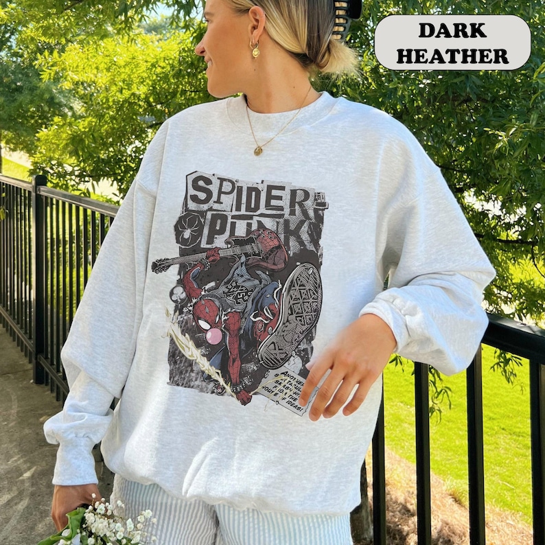Peut inclure: Sweat-shirt gris chin&eacute; fonc&eacute; avec un motif Spider-Punk. Le motif comprend les mots "Spider Punk" et une illustration de Spider-Man jouant de la guitare. Le sweat-shirt a des manches longues et un col rond.