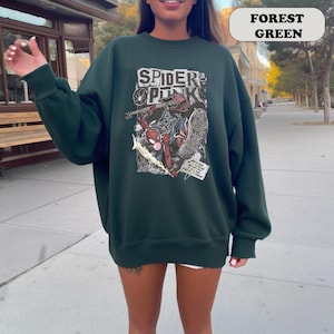 Peut inclure: Sweat-shirt vert for&ecirc;t avec un motif de Spider-Man de style bande dessin&eacute;e et le texte "SPIDER PUNK". Le motif utilise du rouge, du bleu et du blanc. Le sweat-shirt est de couleur unie et a des manches longues.