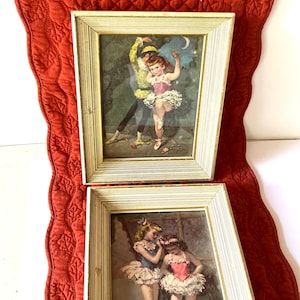 May include: Two framed vintage prints of young ballerinas in antique gold frames. The top print features a ballerina in a pink tutu being lifted by a man in a yellow and black costume. The bottom print features two ballerinas in tutus, one in pink and one in blue, standing together.