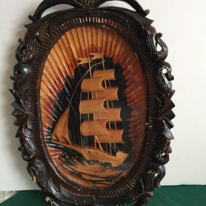 Könnte beinhalten: Eine Holz-Wandplakette mit einer geschnitzten Abbildung eines Schiffes, das auf dem Meer segelt. Die Plakette ist oval geformt und hat einen dunkelbraunen Rahmen mit aufwendigen Schnitzereien.