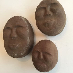 K&ouml;nnte beinhalten: Drei braune Tonskulpturen von Gesichtern mit geschlossenen Augen. Die Skulpturen sind rund und haben eine glatte, strukturierte Oberfl&auml;che.