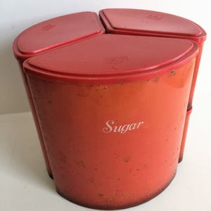 May include: A set of three red ceramic canisters with lids. The canisters are labeled "Sugar", "Flour", and "Tea".