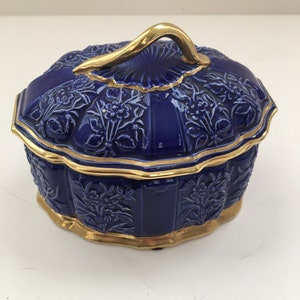 Könnte beinhalten: Eine blaue und goldene Keramik-Schmuckschatulle mit floralem Muster und goldenem Griff.