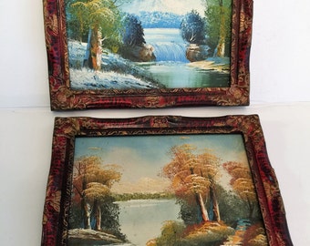 Op de afbeelding: Twee ingelijste landschapschilderijen met sierlijke rode en gouden lijsten. Het bovenste schilderij toont een besneeuwde berg scène met een waterval en een meer. Het onderste schilderij toont een meer scène met bomen in herfstkleuren.