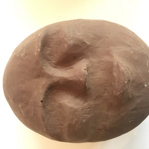 K&ouml;nnte beinhalten: Eine braune Tonskulptur eines Gesichts mit geschlossenen Augen und leicht ge&ouml;ffnetem Mund.