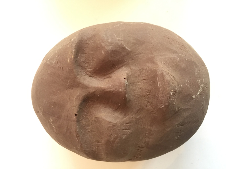 K&ouml;nnte beinhalten: Eine braune Tonskulptur eines Gesichts mit geschlossenen Augen und leicht ge&ouml;ffnetem Mund.