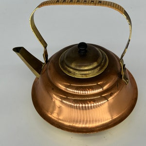 May include: A copper kettle with a brass lid and a wooden handle. The kettle has a rounded body and a spout on the side.