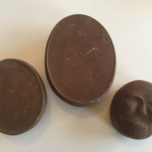 K&ouml;nnte beinhalten: Drei braune Keramik-Wanddekorationen. Zwei sind oval geformt und eine ist ein rundes Gesicht.