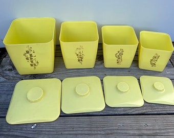 May include: Set of four yellow ceramic canisters with lids. The canisters are labeled "FLOUR", "SUGAR", "COFFEE", and "TEA".