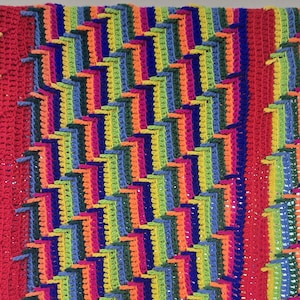 Peut inclure: Une couverture au crochet faite &agrave; la main, aux couleurs vives, avec un motif g&eacute;om&eacute;trique r&eacute;p&eacute;titif. Le design incorpore du rouge, de l'orange, du jaune, du vert, du bleu et du violet, cr&eacute;ant une pi&egrave;ce visuellement frappante et textur&eacute;e. Un &eacute;l&eacute;ment de d&eacute;coration int&eacute;rieure confortable et color&eacute;.