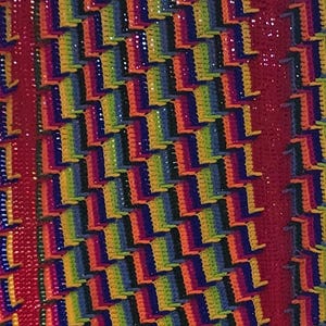 May include: A vibrant, handmade crochet blanket featuring a repeating pattern of colorful blocks in rainbow hues. The blanket has a red border and fringe, creating a cozy and eye-catching textile.