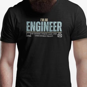 May include: Black t-shirt featuring the text "I'M AN ENGINEER" in light blue, with the phrase "OF COURSE I WRITE CODE AND UNREADABLE EMAILS" below. The design includes a laptop and an email icon.