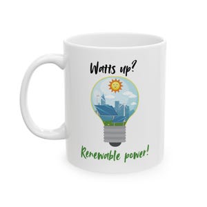 Könnte beinhalten: Weißer Keramikbecher mit Henkel. Der Becher zeigt ein Glühbirnen-Design, das mit einer Stadtlandschaft, Sonnenkollektoren und Windturbinen gefüllt ist, mit dem Text "Watts up?" und "Renewable power!"