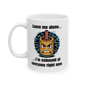 May include: White ceramic mug with a humorous cartoon of an angry solenoid. The solenoid is yellow and brown with a red top, surrounded by blue lightning bolts. Text on the mug reads "Leave me alone... I'm solenoid at everyone right now."