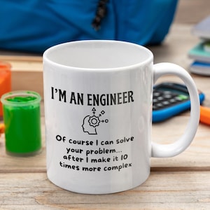 May include: White ceramic mug with the text "I'M AN ENGINEER" and a humorous quote about problem-solving. The mug features a black graphic of a person's head with gears and arrows. The mug is on a wooden surface.