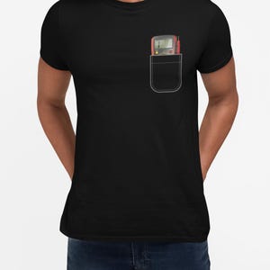 May include: Black t-shirt with a pocket design. The pocket features a digital multimeter with red and black probes. The multimeter has a gray body with a digital display and several buttons. The shirt is a solid black color.