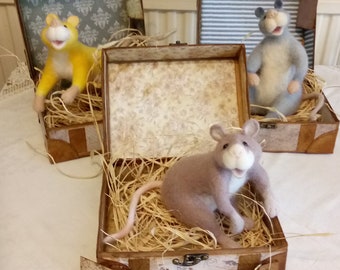 May include: Three vintage suitcases with handles, each containing a different stuffed animal. The first suitcase has a yellow stuffed animal, the second has a gray stuffed animal, and the third has a light blue stuffed animal. The suitcases are on a white tablecloth with a lace trim.