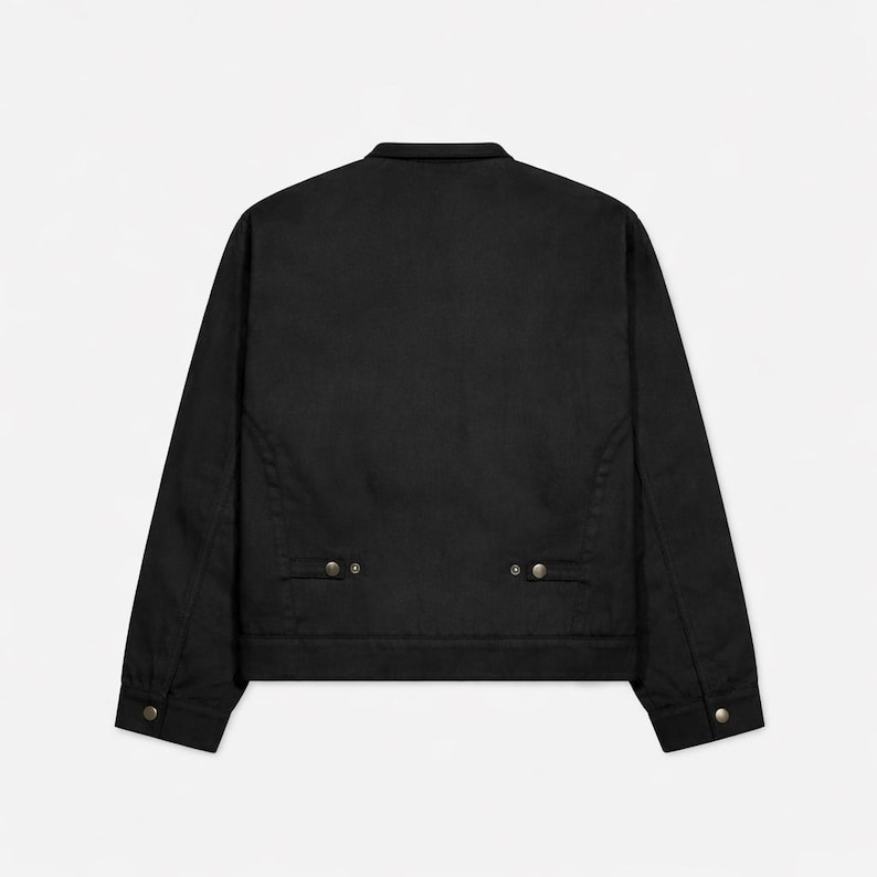May include: A black jacket with a collar and long sleeves. The jacket has two small pockets near the waist and button closures on the cuffs. The back of the jacket is plain and the fabric appears to be a sturdy material.