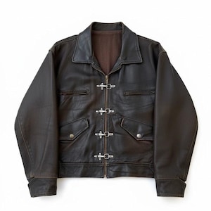May include: A dark brown leather jacket with a collar, zip fastening, and four decorative clasps. The jacket features two chest pockets and two lower pockets with snap closures. The interior lining is a lighter brown colour.