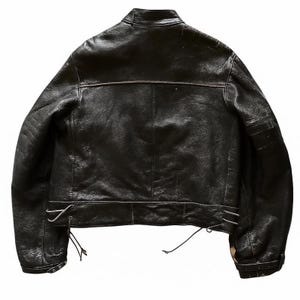 May include: Black leather jacket with a classic design. Features include a stand-up collar, a horizontal seam across the upper back, and adjustable side laces. The jacket has a slightly distressed appearance.