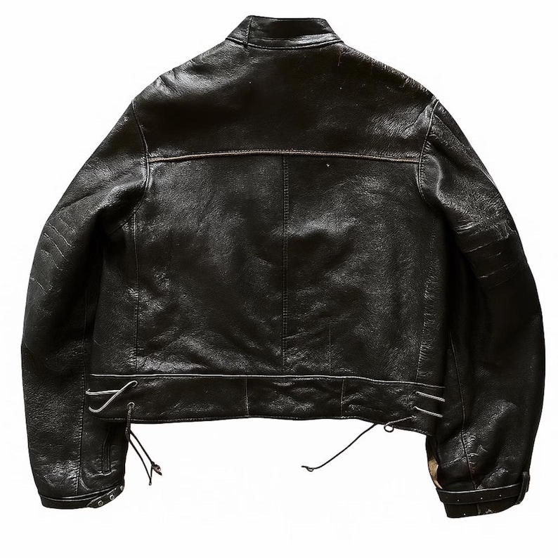May include: Black leather jacket with a classic design. Features include a stand-up collar, a horizontal seam across the upper back, and adjustable side laces. The jacket has a slightly distressed appearance.