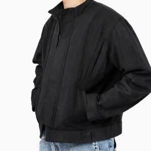 May include: Black jacket with a stand-up collar, front zipper, and side pockets. The jacket has a ribbed design on the front and a straight hem. The sleeves are long and the jacket is made of a durable material.