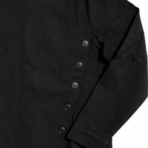 May include: Black long-sleeved shirt with a high collar and button details. The shirt features a series of buttons down the front and on the collar. The fabric appears to be a solid, dark color.