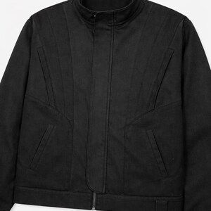 May include: Black jacket with a stand-up collar and a full-length zipper. The jacket features angled seams and two front pockets. The jacket is made of a solid black material.