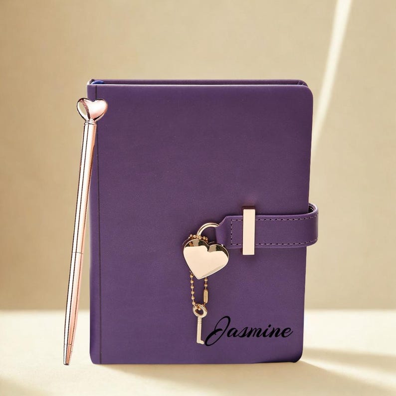 May include: A purple journal with a heart-shaped lock and a matching pen. The journal has a strap closure and the name "Jasmine" printed on the front. The pen and lock are gold-colored.
