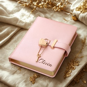 May include: A pink diary with a heart-shaped lock and key. The diary has a strap closure and the name "Olivia" is printed on the cover. The edges of the pages are gold.