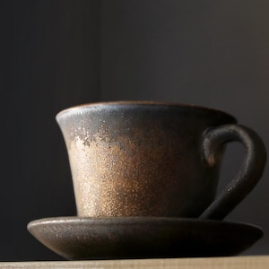 Puede incluir: Una taza de cerámica blanca con un asa negra y el texto "But First, Coffee" en negro y negrita. La taza está sobre una superficie blanca. La taza mide aproximadamente 10 cm de alto.