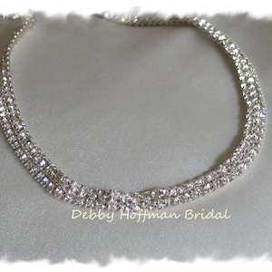 May include: A silver necklace with three rows of sparkling rhinestones. The necklace is on a white background.