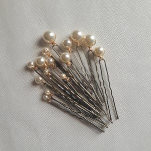 May include: A set of gold hair pins with pearl accents. The pins are arranged in a fan shape, with the pearls facing outward.