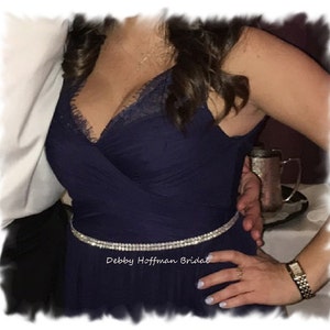 May include: A navy blue, strapless dress with a lace bodice and a sparkly belt. The dress has a flowing skirt and is cinched at the waist. The text "Debby Hoffman Bridal" is visible on the belt.