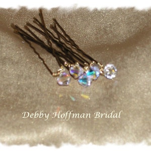 May include: A set of gold hair pins with clear crystal accents. The pins are arranged on a beige fabric background.