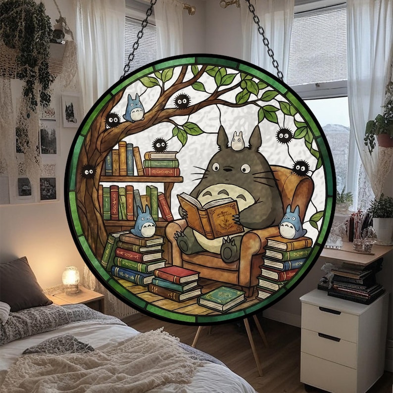 Pode incluir: Vitral redondo com um personagem de desenho animado, Totoro, lendo um livro. A cena inclui uma estante, outros personagens e uma &aacute;rvore, tudo dentro de uma moldura verde.