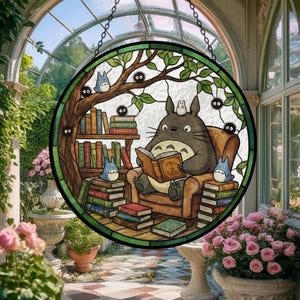 Pode incluir: Vitral redondo com um personagem de desenho animado Totoro lendo um livro. A cena inclui uma estante, outros personagens e uma &aacute;rvore, tudo dentro de uma moldura verde e marrom.