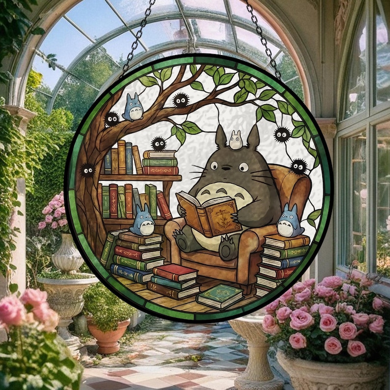 Pode incluir: Vitral redondo com um personagem de desenho animado Totoro lendo um livro. A cena inclui uma estante, outros personagens e uma &aacute;rvore, tudo dentro de uma moldura verde e marrom.