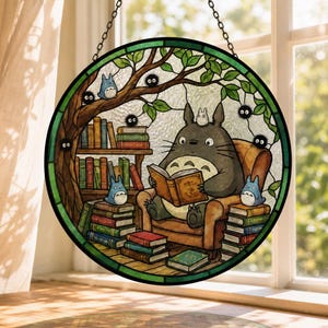 Pode incluir: Vitral redondo com uma cena de desenho animado. Um grande personagem cinzento l&ecirc; um livro numa cadeira, rodeado por personagens azuis mais pequenos e livros. A cena passa-se sob uma &aacute;rvore com folhas verdes.