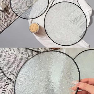 Pode incluir: Tr&ecirc;s espelhos redondos de vidro texturizado com molduras de metal preto pendurados em correntes pretas. Os espelhos s&atilde;o exibidos em uma superf&iacute;cie branca com jornal e uma vela. Decora&ccedil;&atilde;o para casa.