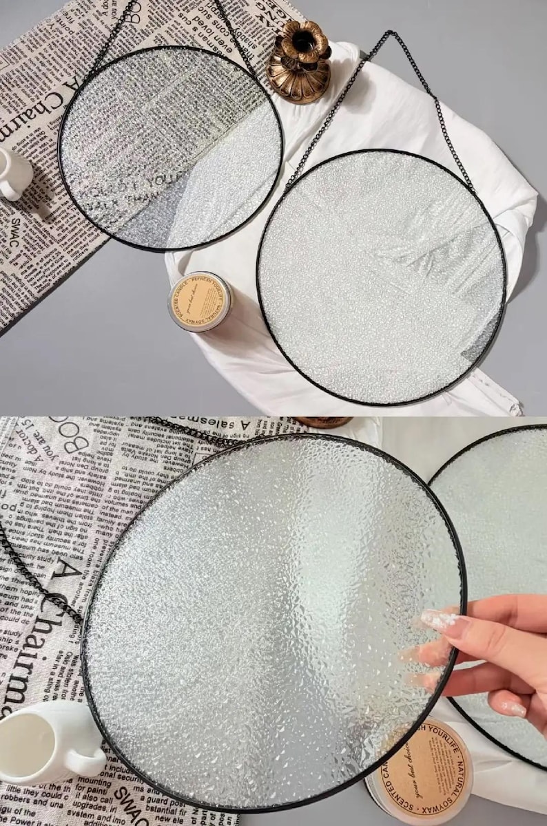 Pode incluir: Tr&ecirc;s espelhos redondos de vidro texturizado com molduras de metal preto pendurados em correntes pretas. Os espelhos s&atilde;o exibidos em uma superf&iacute;cie branca com jornal e uma vela. Decora&ccedil;&atilde;o para casa.