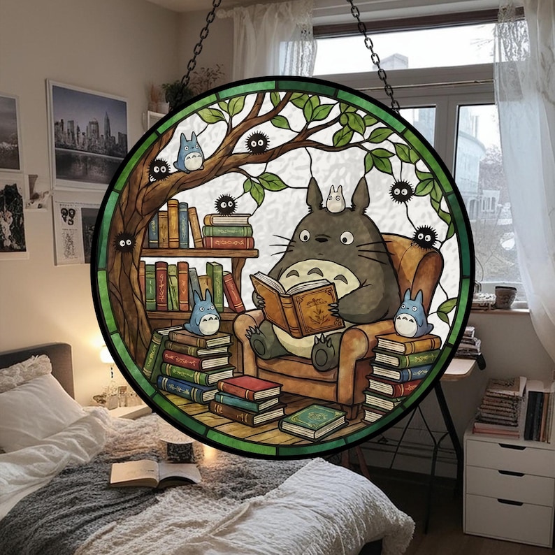Pode incluir: Vitral redondo com Totoro lendo um livro, rodeado por livros e personagens do filme de anima&ccedil;&atilde;o. O design inclui uma &aacute;rvore e &eacute; emoldurado com uma borda preta. Ele pende de uma corrente.