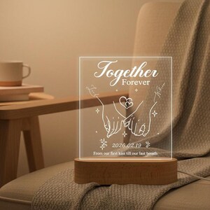 May include: A clear acrylic LED night light with the words "Together Forever" and a graphic of two hands holding each other. The light sits on a wooden base and includes the date 2026.02.19 and the phrase "From our first kiss till our last breath."