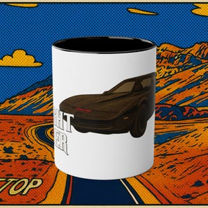 May include: White ceramic mug with a black interior and a graphic of a black sports car with the text "NIGHT RIDER". The mug has a pop art style design with a blue sky and orange mountains in the background.
