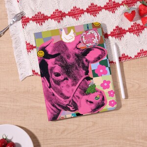 Könnte beinhalten: Eine pinke und schwarze Tablet-Hülle mit einem Kuhgesicht im Pop-Art-Stil, einem Frosch mit Cowboyhut, einer Discokugel und einem Huhn. Die Hülle hat einen bunten karierten Hintergrund mit rosa Blumen und einem Smiley.