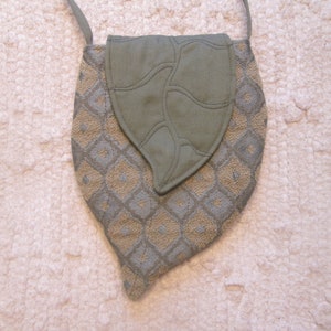 May include: A gray and beige leaf-shaped fabric handbag with a geometric pattern. The bag has a long strap and a flap closure.