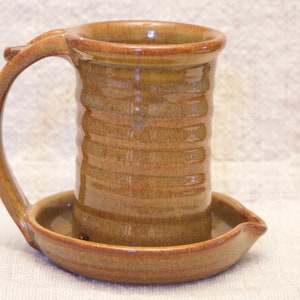 May include: A brown ceramic mug with a handle and a matching saucer. The mug has a textured, striped design.