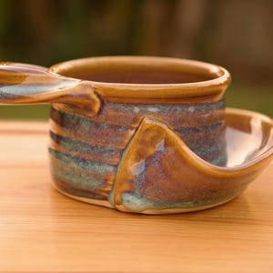 May include: A brown and blue ceramic cup with a handle and a matching saucer. The cup and saucer have a striped pattern.