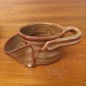 以下が含まれることがあります： 側面に注ぎ口と持ち手のある茶色の陶器製のマグカップ。マグカップは斑点のある釉薬がかかっています。